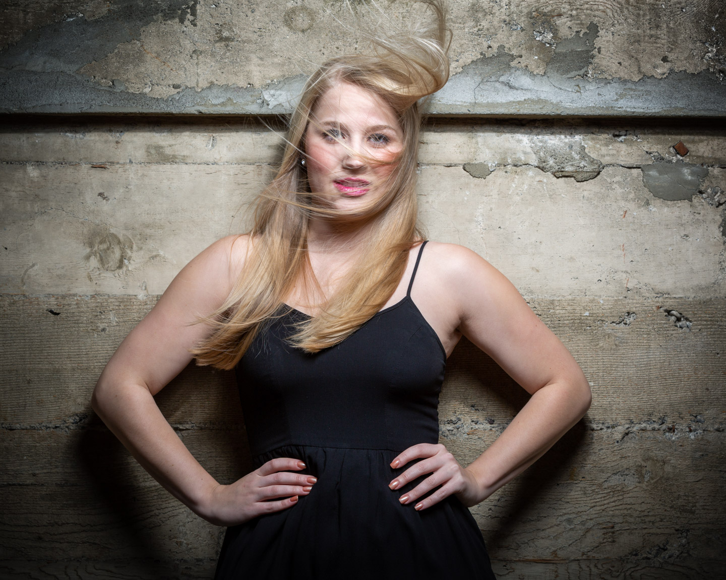 A woman in a black dress, hair caught in motion, standing with quiet confidence